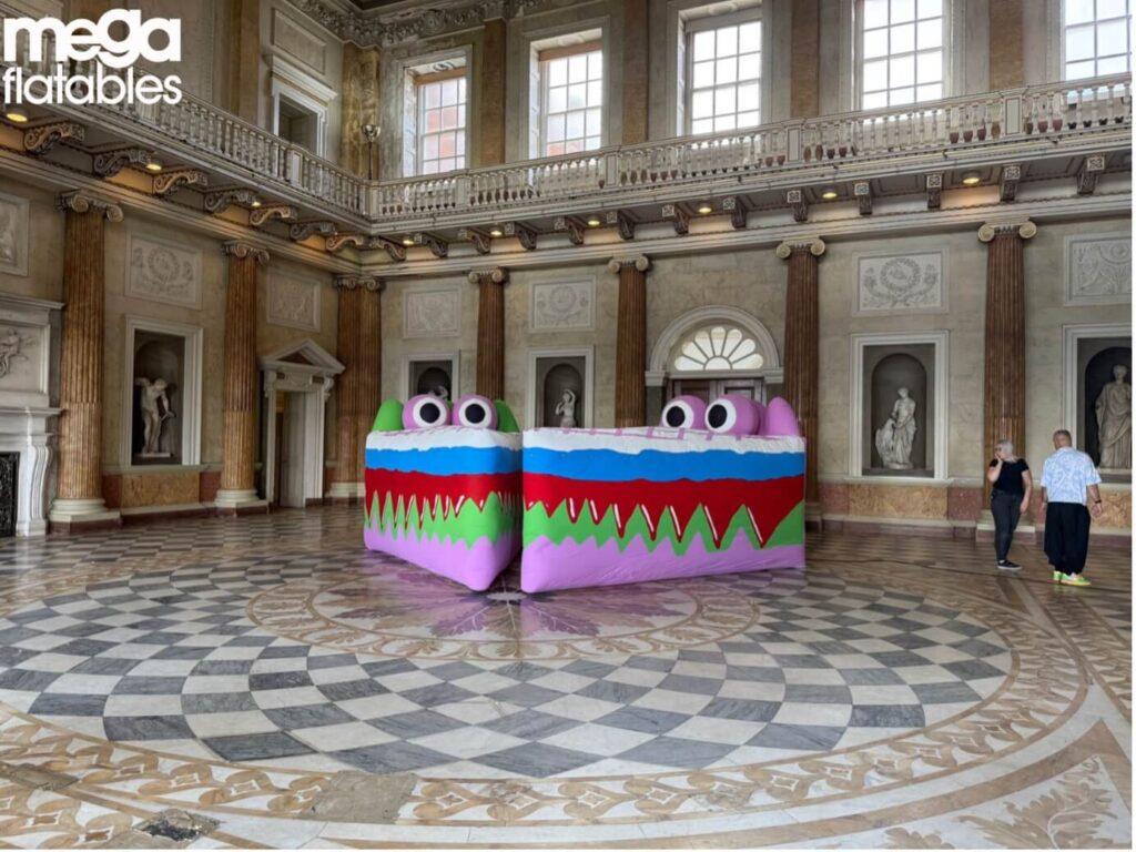 large colourful inflatable monster installation with big eyes displayed inside an ornate historic hall with marble floors and classical statues